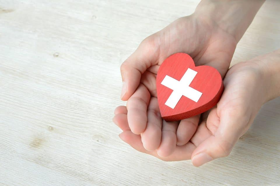 Hands holding red heart with white cross on it